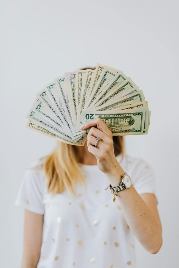 Woman holding a fan of US dollar bills in front of her face.