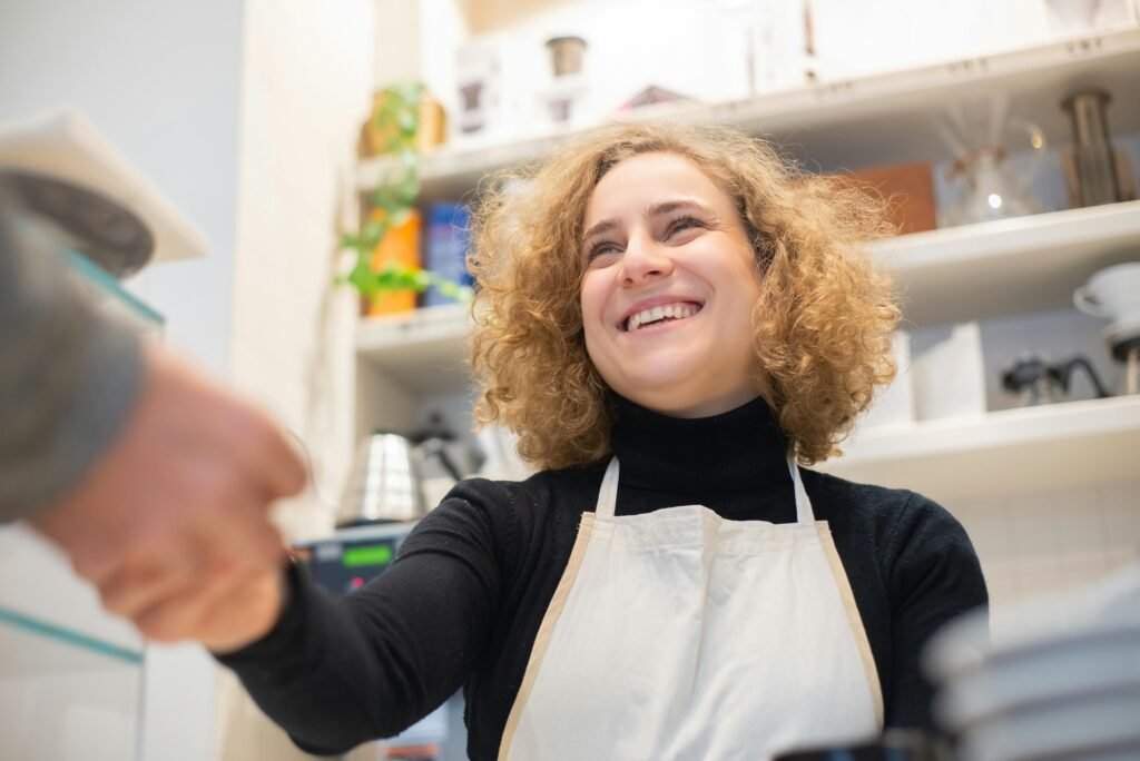 Smiling barista in café, engaging positively with customer, signifying hospitality.
