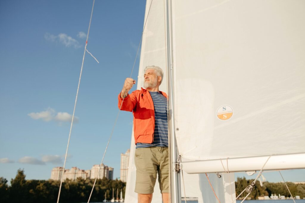 A senior man confidently sailing, looking ahead under a clear blue sky.